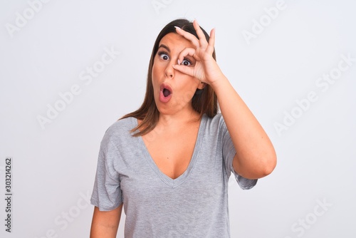 Portrait of beautiful young woman standing over isolated white background doing ok gesture shocked with surprised face, eye looking through fingers. Unbelieving expression.