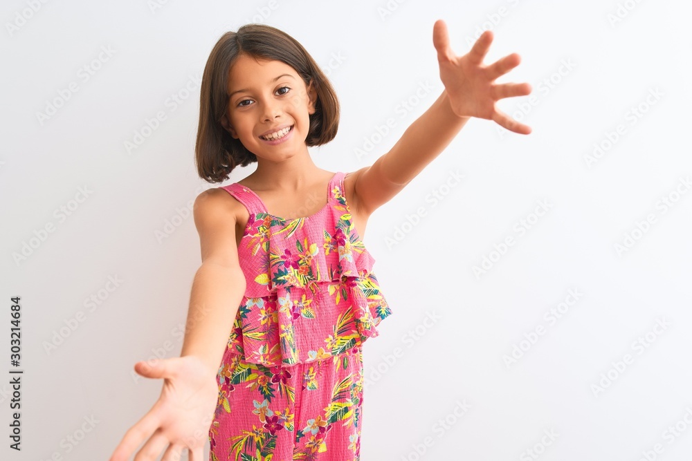 Young beautiful child girl wearing pink floral dress standing over isolated white background looking at the camera smiling with open arms for hug. Cheerful expression embracing happiness. Young beautiful child girl wearing pink floral dress standing over isolated white background looking at the camera smiling with open arms for hug. Cheerful expression embracing happiness.
