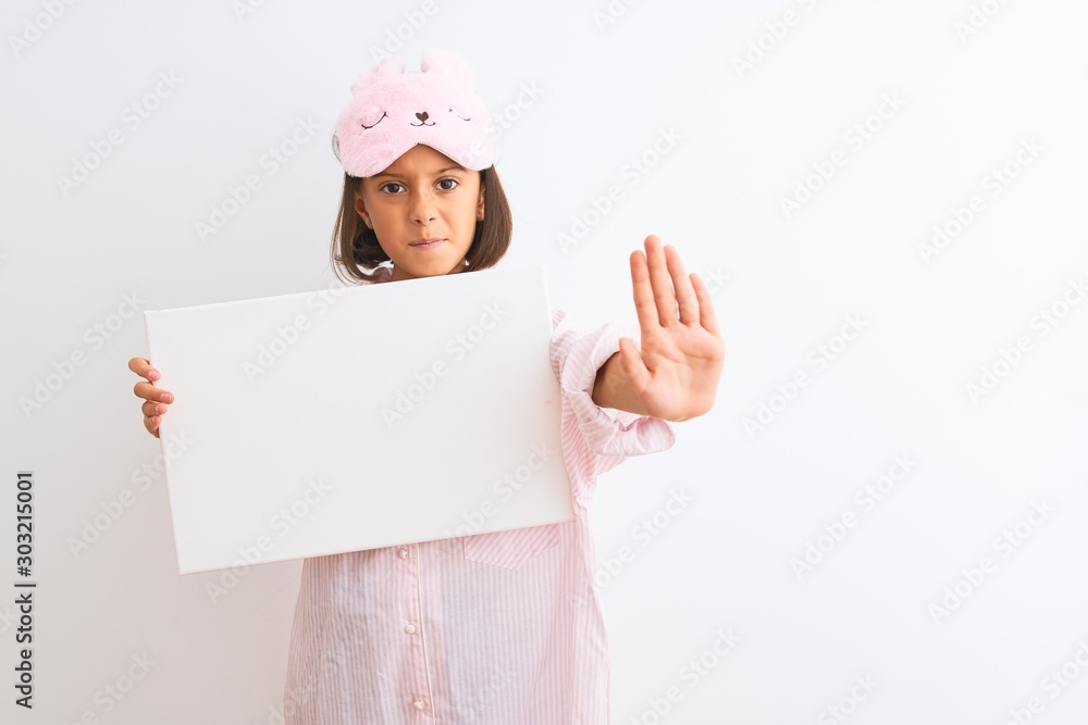 Child girl wearing sleep mask and pajama holding banner over isolated white background with open hand doing stop sign with serious and confident expression, defense gesture Child girl wearing sleep mask and pajama holding banner over isolated white background with open hand doing stop sign with serious and confident expression, defense gesture