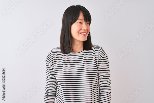 Young beautiful chinese woman wearing black striped t-shirt over isolated white background looking away to side with smile on face, natural expression. Laughing confident.