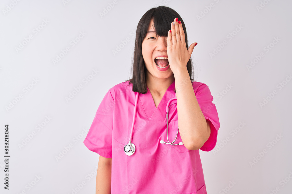 Young beautiful Chinese nurse woman wearing stethoscope over isolated white background covering one eye with hand, confident smile on face and surprise emotion. Young beautiful Chinese nurse woman wearing stethoscope over isolated white background covering one eye with hand, confident smile on face and surprise emotion.