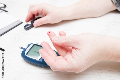 female hand with a drop of blood on a finger, measuring blood sugar, diabetes concept, glucose meter in the back.