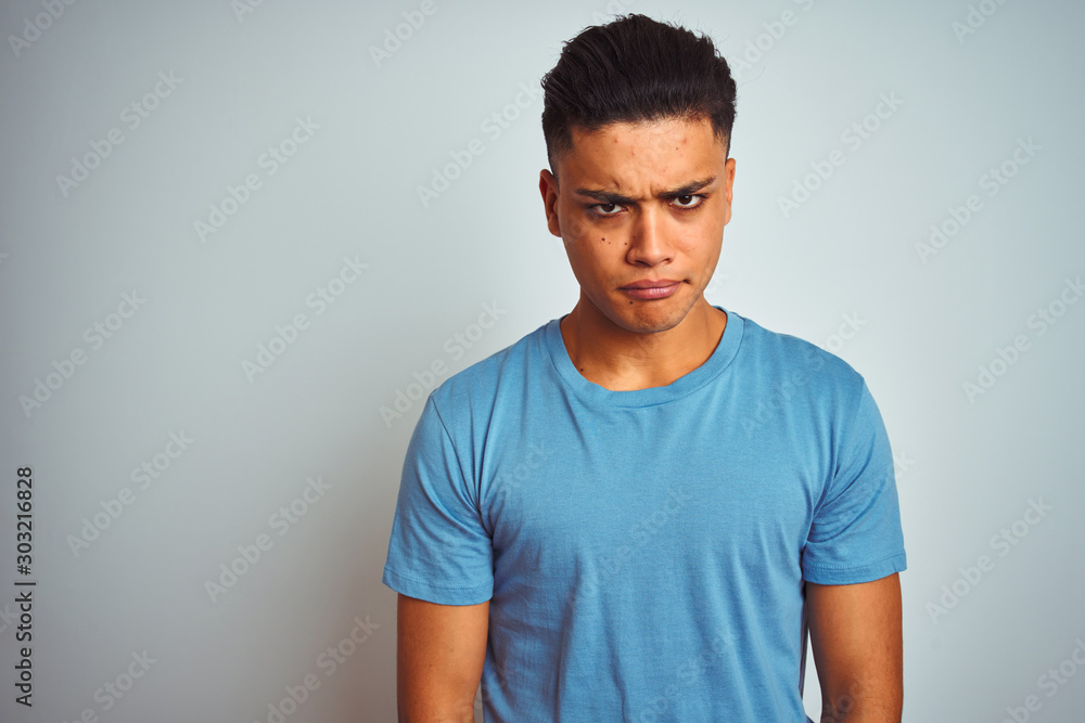 Obraz premium Young brazilian man wearing blue t-shirt standing over isolated white background skeptic and nervous, frowning upset because of problem. Negative person.