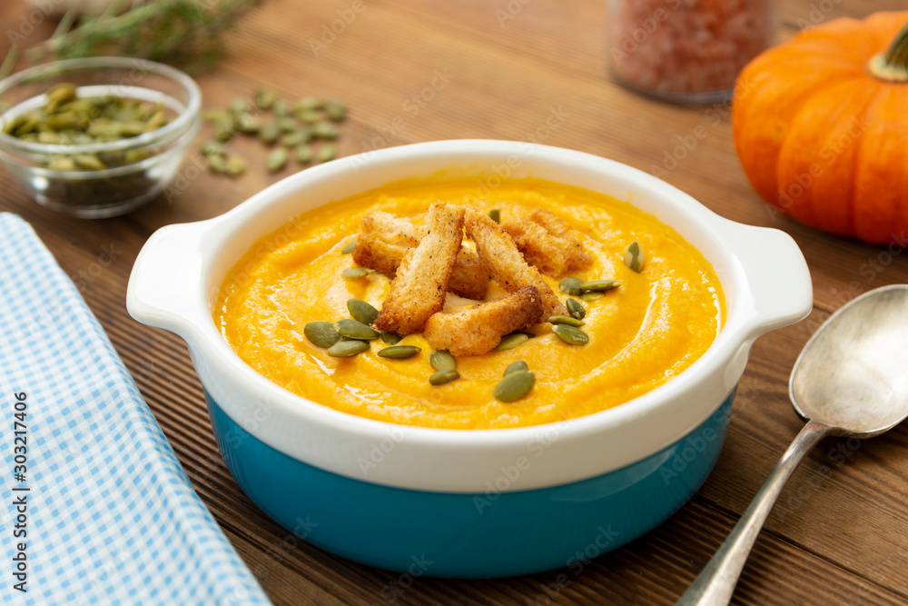 Pumpkin soup in a bowl,with fresh pumpkin seeds. Autumn foods. Healthy, vegetarian food, wooden background. Pumpkin soup in a bowl,with fresh pumpkin seeds. Autumn foods. Healthy, vegetarian food, wooden background.