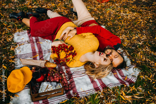 Young loving couple in the autumn park have a rest lying on a plaid, an autumn picnic with wine and fruits.