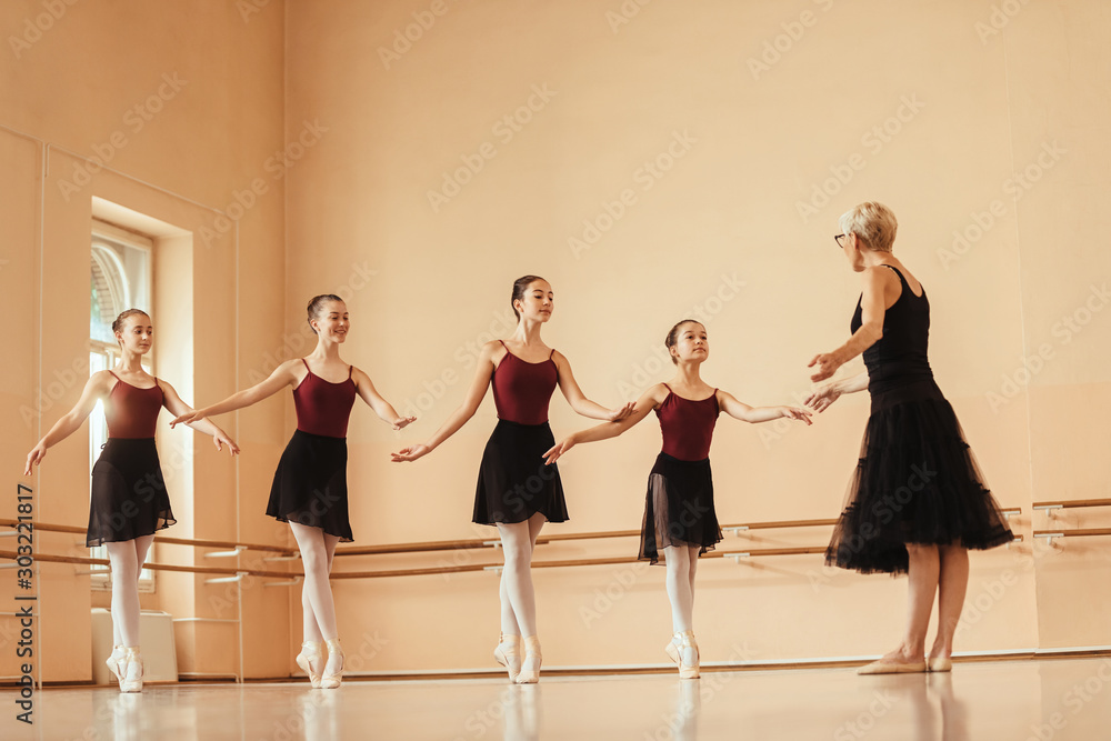 Naklejka premium Graceful ballerinas practicing with mature instructor at ballet studio.