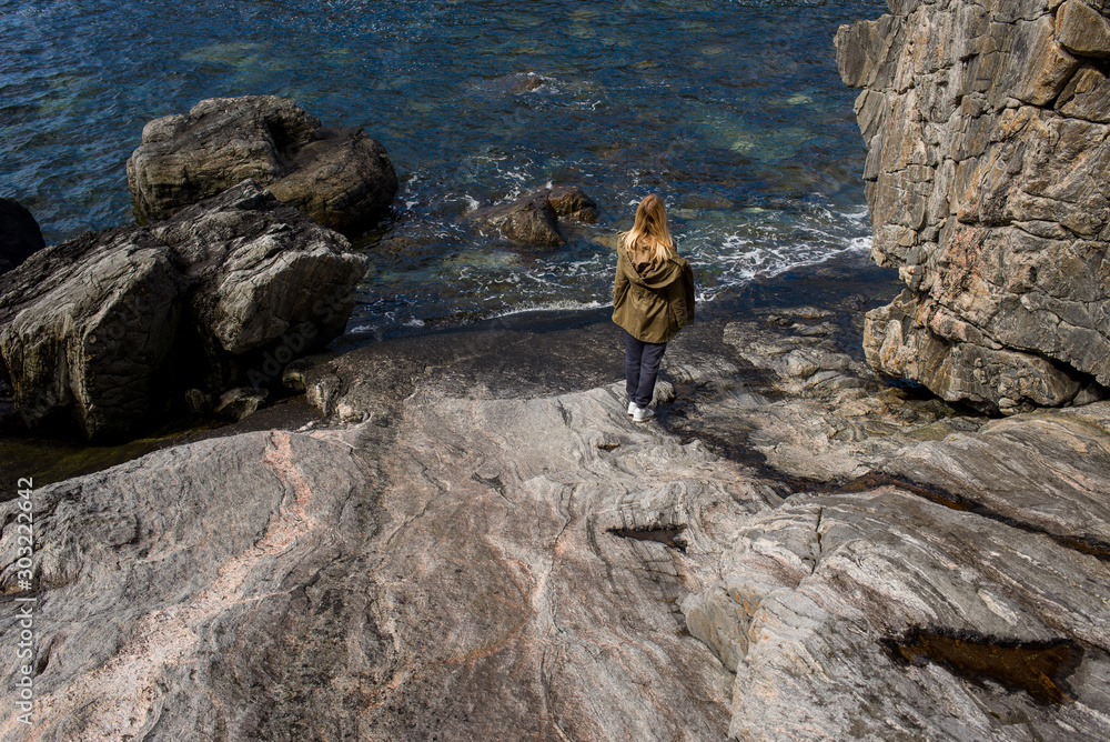 A girl walks on the stones of coastline near the ocean. Beautiful nature landscape in North. Scenic outdoor view. Enjoy the moment, relaxation. Wanderlust. Travel, adventure, lifestyle. Explore Norway