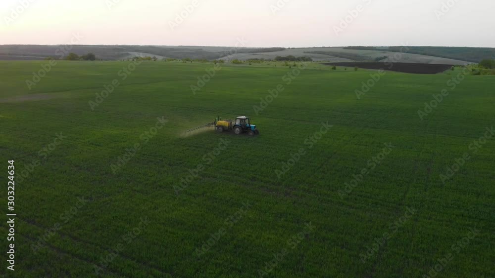 Aerial view of farming tractor spraying on field with sprayer, herbicides and pesticides at sunset. Farm machinery spraying insecticide to the green field, agricultural natural seasonal spring works. Aerial view of farming tractor spraying on field with sprayer, herbicides and pesticides at sunset. Farm machinery spraying insecticide to the green field, agricultural natural seasonal spring works.
