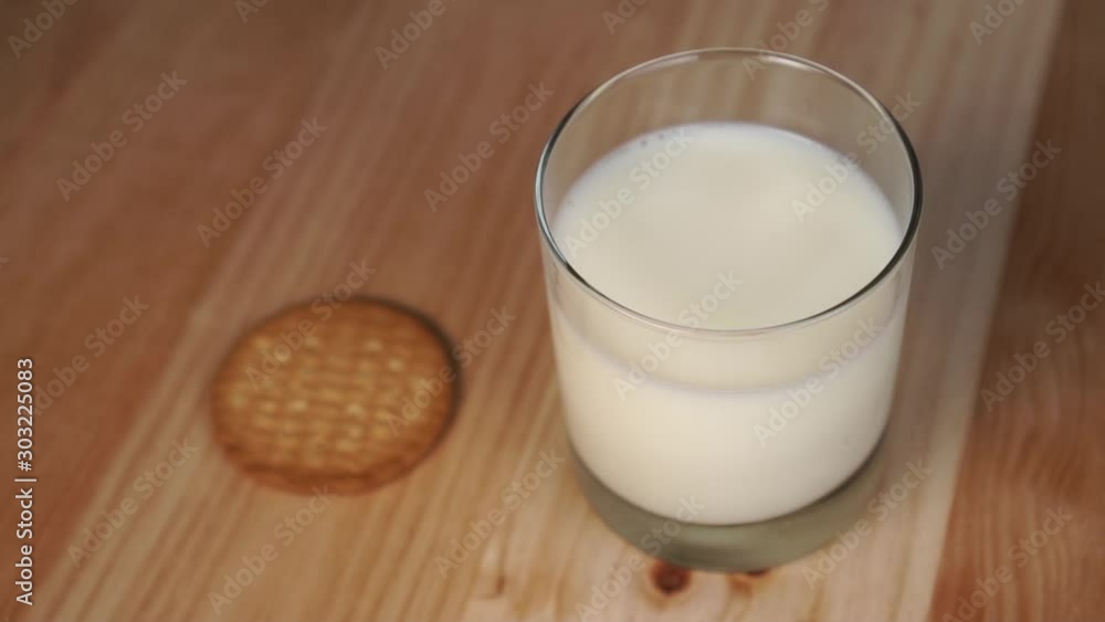 Round oatmeal cookies fall on a wooden table next to a glass of milk. Slow motion. Healthy breakfast of herbal products Round oatmeal cookies fall on a wooden table next to a glass of milk. Slow motion. Healthy breakfast of herbal products
