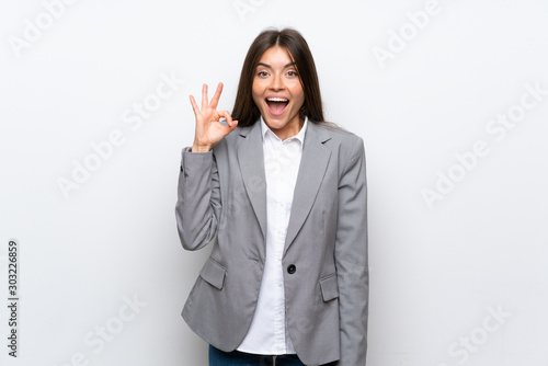 Young business woman over isolated white background surprised and showing ok sign