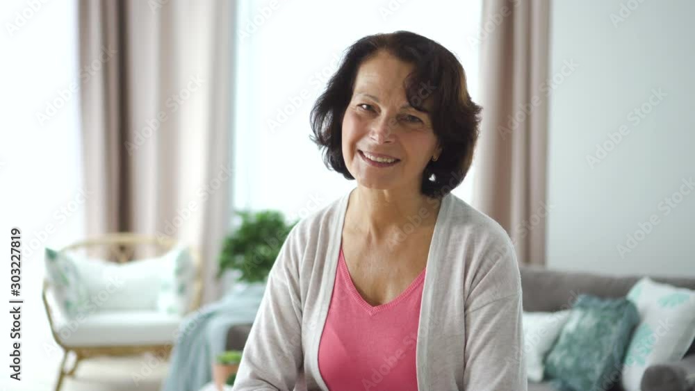 60s Happy elderly woman watching front sitting at sofa in home room. 4k Portrait of retired american female is having fun and smiling at couch on window background in apartment. Attractive 60s 60s Happy elderly woman watching front sitting at sofa in home room. 4k Portrait of retired american female is having fun and smiling at couch on window background in apartment. Attractive 60s