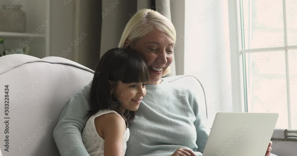Happy mature grandma and curious little granddaughter using laptop Happy mature grandma and curious little granddaughter using laptop