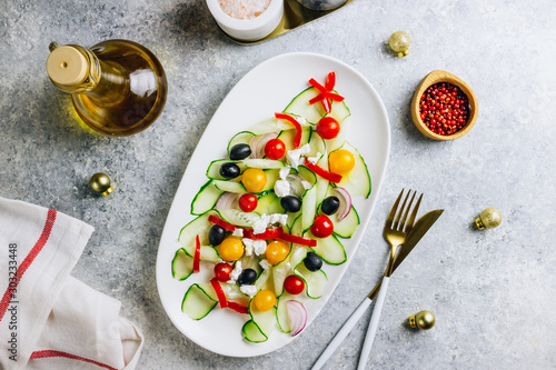Vegetable Greek salad with tomatoes, feta cheese, onions, cucumber and olives. christmas tree shape. Served on white plate on the festive table. Top view. Flat lay. Copy space