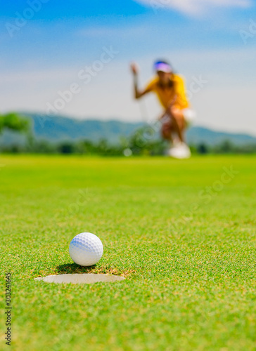 golf ball run through almost success drop to hole on the green with exciting watching by woman golf player in background