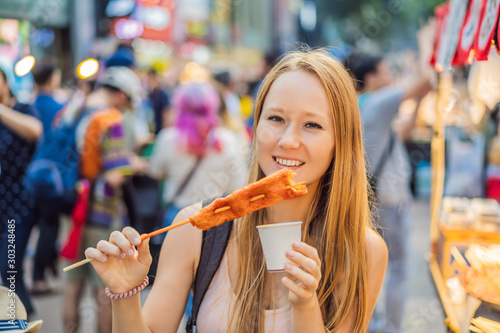 Photography Young woman tourist eating Typical Korean street food on a walking street of Seoul