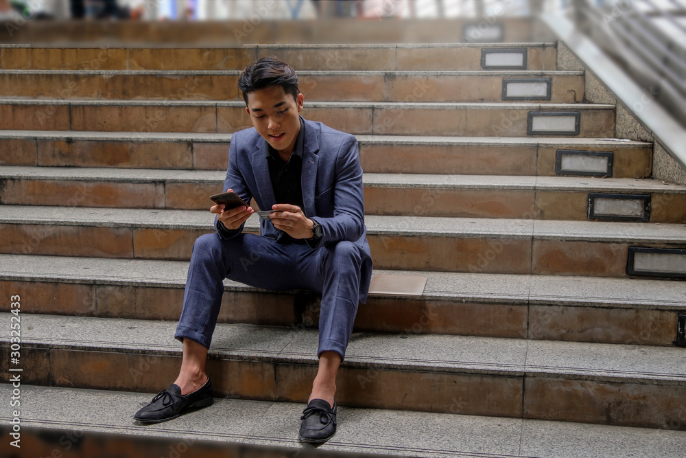 Young business man using credit card for online payment via mobile phone, sitting at stairs at city Young business man using credit card for online payment via mobile phone, sitting at stairs at city