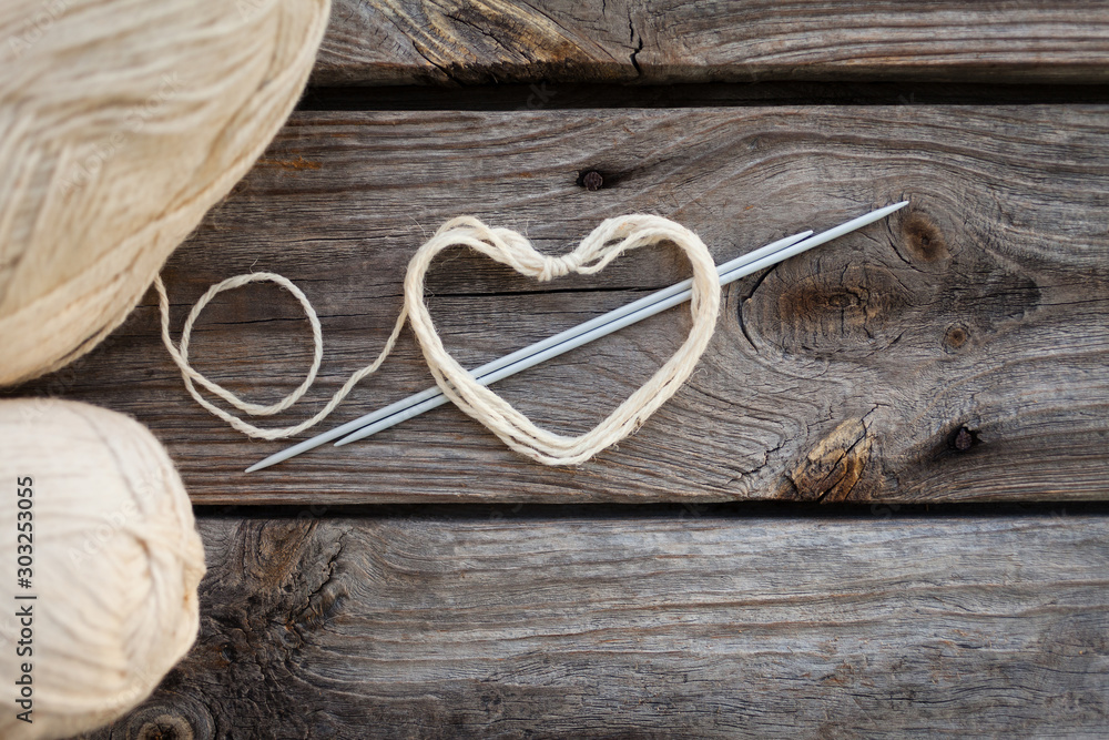 White knitting wool and knitting needles with heart. Wooden background, natural wool knitting background White knitting wool and knitting needles with heart. Wooden background, natural wool knitting background
