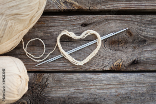 White knitting wool and knitting needles with heart. Wooden background, natural wool knitting background