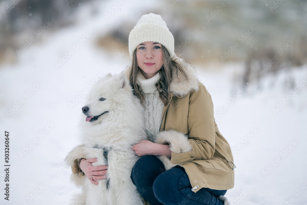 A young girl walks in winter with a white Samoyed dog in a snowy meadow in the forest. A young girl walks in winter with a white Samoyed dog in a snowy meadow in the forest.