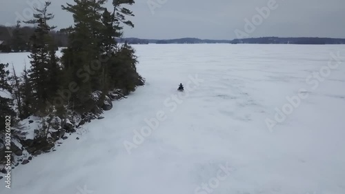 Aerial drone view flying over frozen ice lake Following Snowmobile Rider In Winter