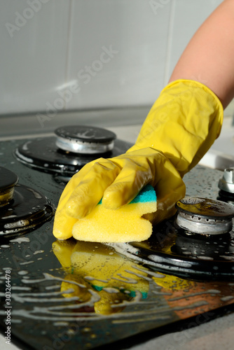 In a yellow rubber glove, a hand cleans a gas stove. Kitchen cleaning