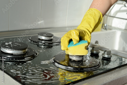 In a yellow rubber glove, a hand cleans a gas stove. Kitchen cleaning