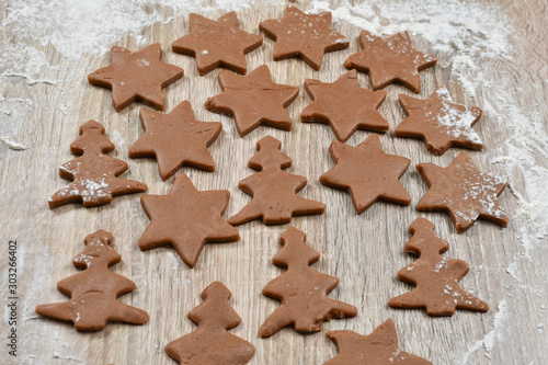 Unrolled spiced dough sliced ​​in cookie cutters on baking paper on a wooden table. Christmas, winter, new year. Fir-trees, stars, flour.