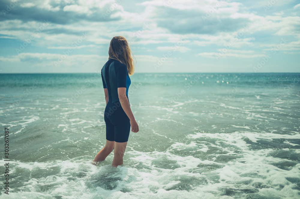 Young woman in wetsuit is standing on the beach with waves crashing in Young woman in wetsuit is standing on the beach with waves crashing in