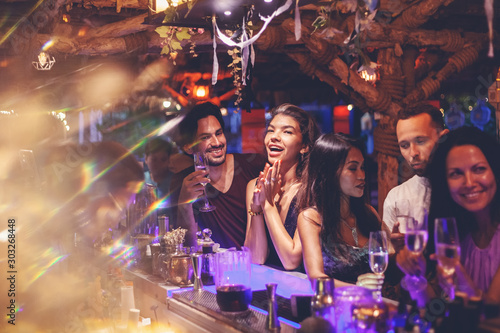 A party of friends in a nightclub at the bar, glamorous young people relax with alcohol.