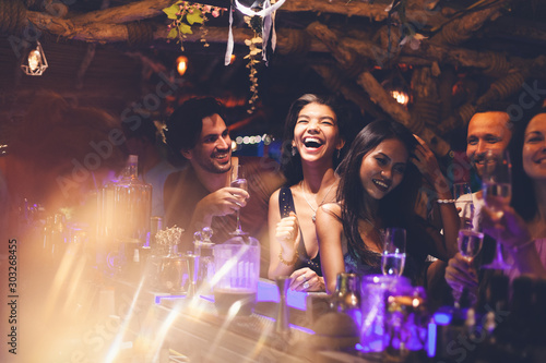 Fotografia A party of friends in a nightclub at the bar, glamorous young people relax with alcohol