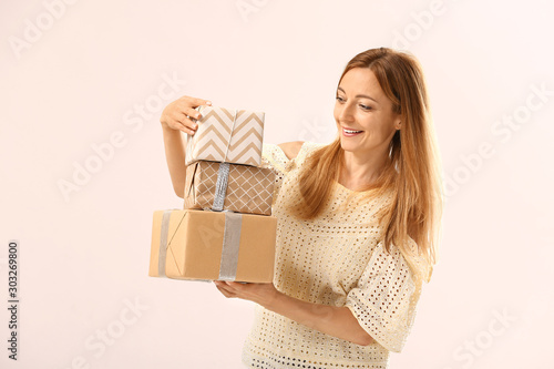 Beautiful woman with gifts on light background