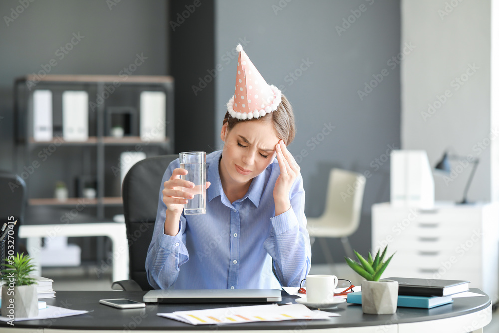 Young woman suffering from hangover in office - obrazy, fototapety, plakaty 