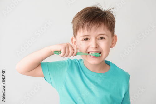 Portrait of little boy brushing teeth on light background
