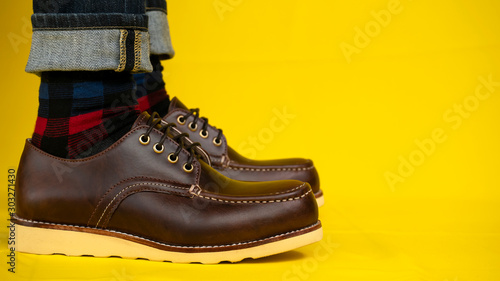 Men fashion with brown shoes leather and jeans on yellow background.