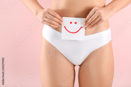 Young woman holding paper with drawn happy emotion on color background. Gynecology concept photo