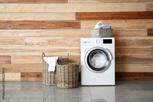 Modern washing machine with laundry near wooden wall photo