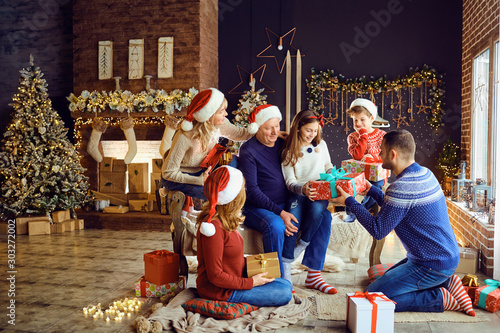 A big family in a room gives gifts at Christmas.