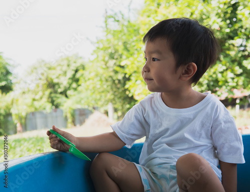 Asian child boy playing sand in sandbox with happy face outdoor with rural natural background. Family relax and freedom time in summer holiday. 