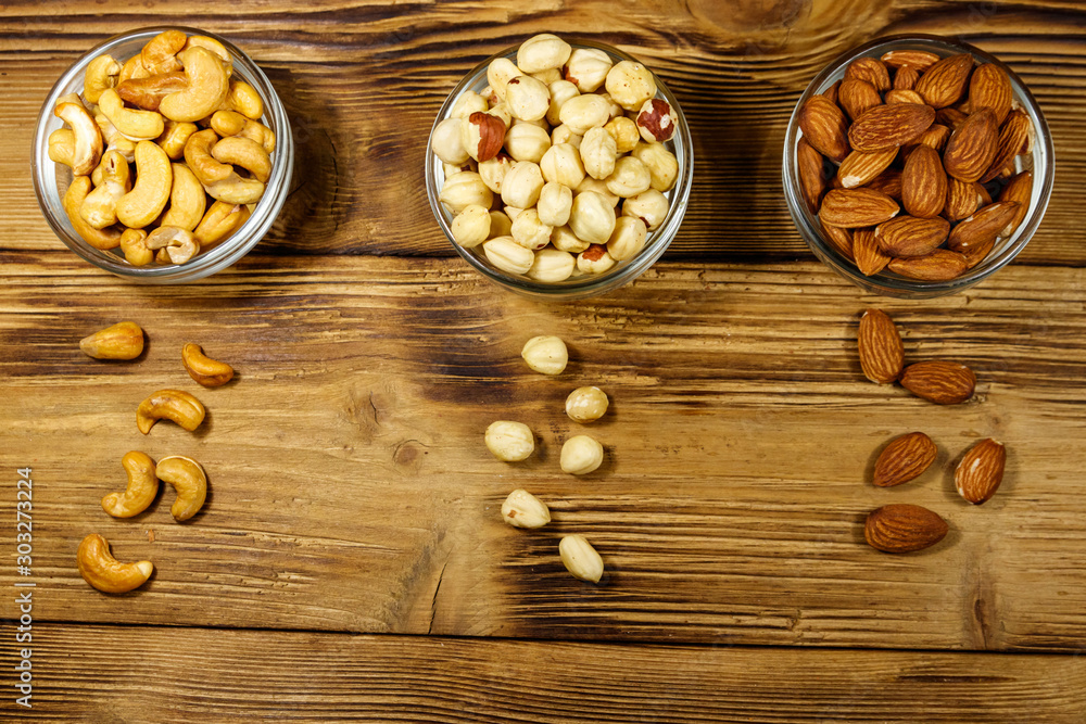 Assortment of nuts on wooden table. Almond, hazelnut and cashew in glass bowls. Top view. Healthy eating concept Assortment of nuts on wooden table. Almond, hazelnut and cashew in glass bowls. Top view. Healthy eating concept