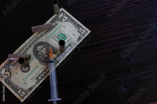 the dollar note, syringe ,blank bullet on brown wood in dark tone.dark or undergroung illegal  business concept photo