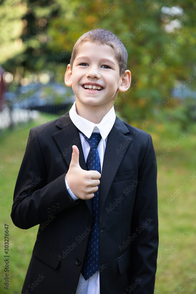 First grade pupil goes to school in a black suit and tie, white shirt. First time to school. Happy boy First grade pupil goes to school in a black suit and tie, white shirt. First time to school. Happy boy