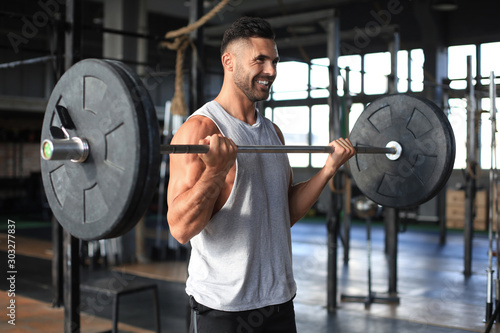 Fotografia Muscular man working out in gym doing exercises with barbell at biceps