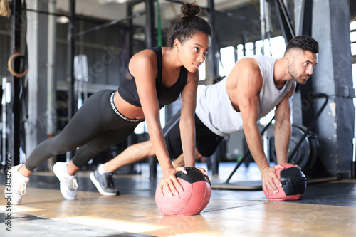 Beautiful young sports couple is working out with medicine ball in gym.