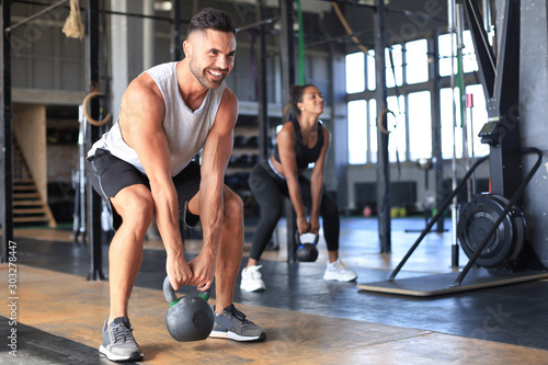 Fit and muscular couple focused on lifting a dumbbell during an exercise class in a gym.