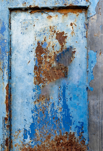A section of a rusty, corroded, and worn steel sliding gate in front of a residential community.