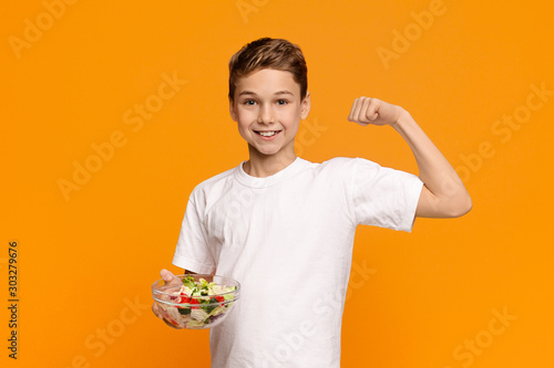 Teen boy with fresh vegetable salad demonstrating his biceps