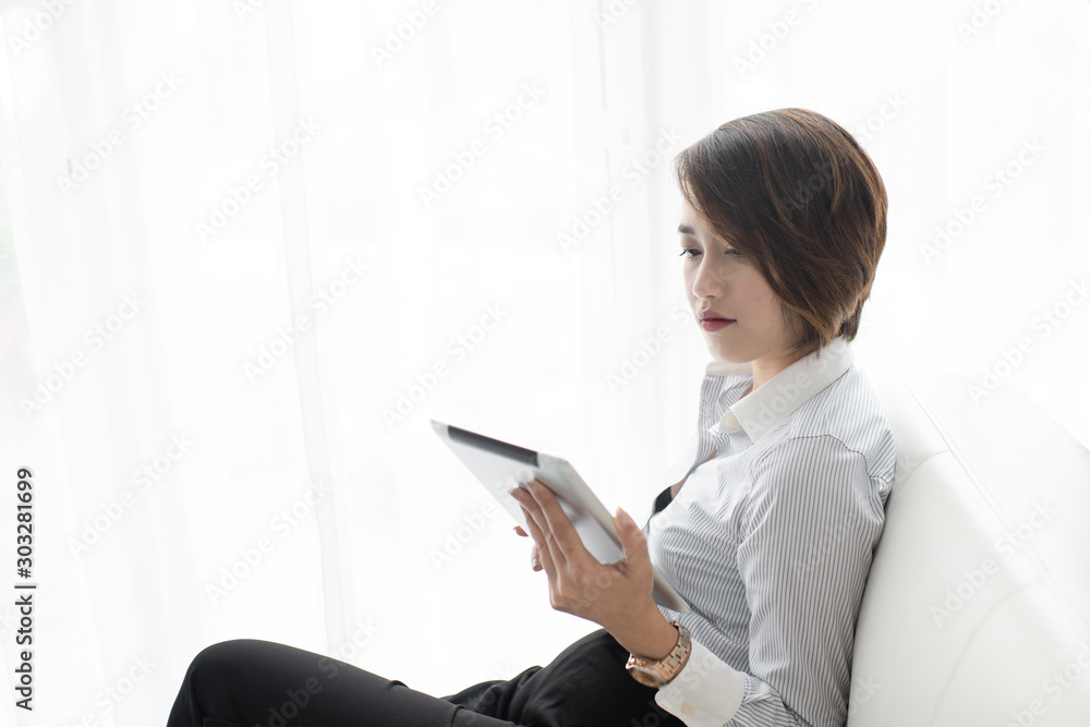 Portrait of a happy Asian woman sitting on sofa using Digital Tablet near window at home. Portrait of a happy Asian woman sitting on sofa using Digital Tablet near window at home.