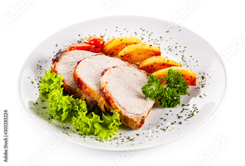 Roasted pork with baked potatoes and vegetables on white plate