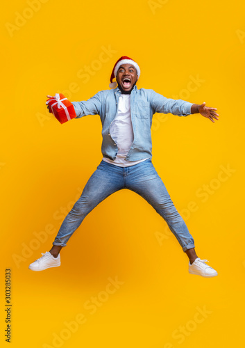 Overjoyed afro guy in santa hat jumping with gift box