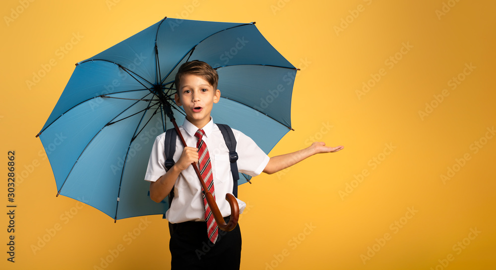 Child student with blue umbrella on yellow background. Amazed expression - obrazy, fototapety, plakaty 